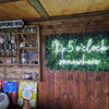 Shed bar with a "It's 5 o-clock somewhere" white neon bar sign and plant wall.