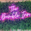 Pink "The bumble in" custom neon bar sign on plant wall.