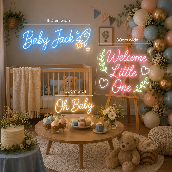 A styled baby shower or nursery party scene with neon sign lights mounted on a wall and on a table. The signs read 'Baby Jack', 'Welcome Little One', and 'Oh Baby' in glowing blue, pink, and yellow lettering.