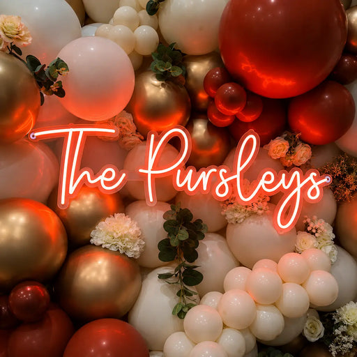 A decorative balloon wall arrangement in red, white, and metallic gold, with small white flowers and greenery, overlaid by the neon-style text 'The Pursleys'.
