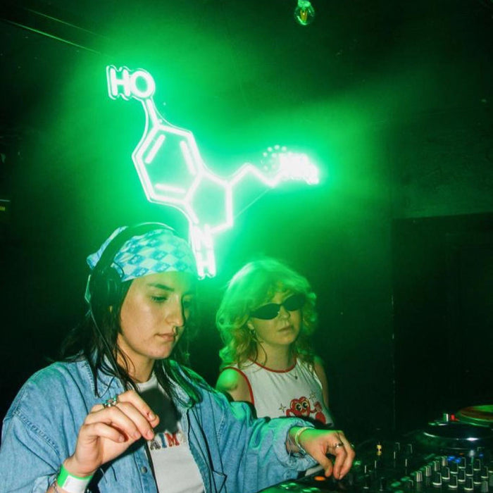 Two women DJing in front of a green Serotonin Neon Sign by clubserotone