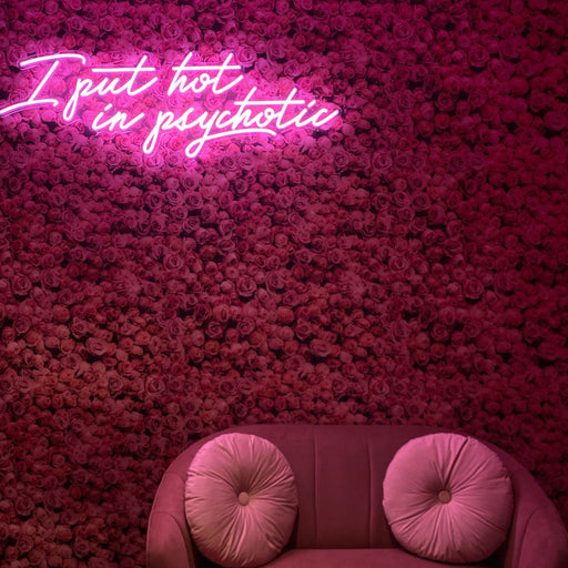 I Put Hot In Psychotic Neon Sign in pastel pink against a pink flowery wall.