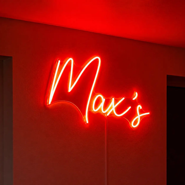 A glowing red neon-style wall sign reading “Max’s” mounted on a red wall in a dim interior.