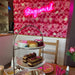 Cream tea on table in front of a pink flower wall with a pink Stay Weird Neon Sign by cakesadaisy