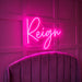 A bright pink neon sign spelling the word 'Reign' in cursive script, mounted on a dark paneled wall above a purple velvet upholstered chair.