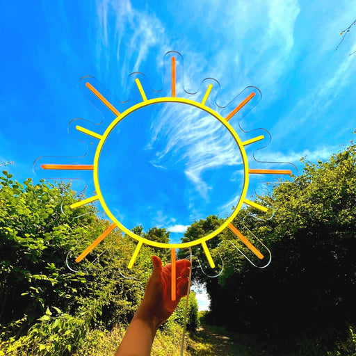 Sun Neon Sign outside. There are green trees and blue summer sky behind it.