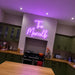 A pink neon sign reading 'The Murrels' mounted on a wall in a modern kitchen with green cabinets and a wooden countertop.