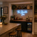 A glowing blue neon sign reading 'The Stumble Inn' mounted on a back wall above a home bar setup with bottles, plants, shelves, and stools in a warm, modern interior.