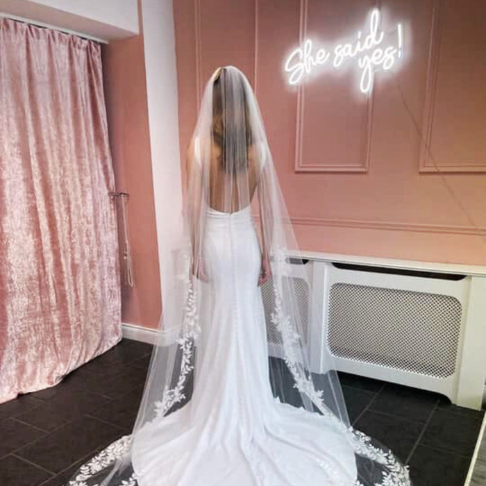 Woman in wedding dress looking away with a white She Said Yes Neon Sign on the wall by pearlsandlacebb