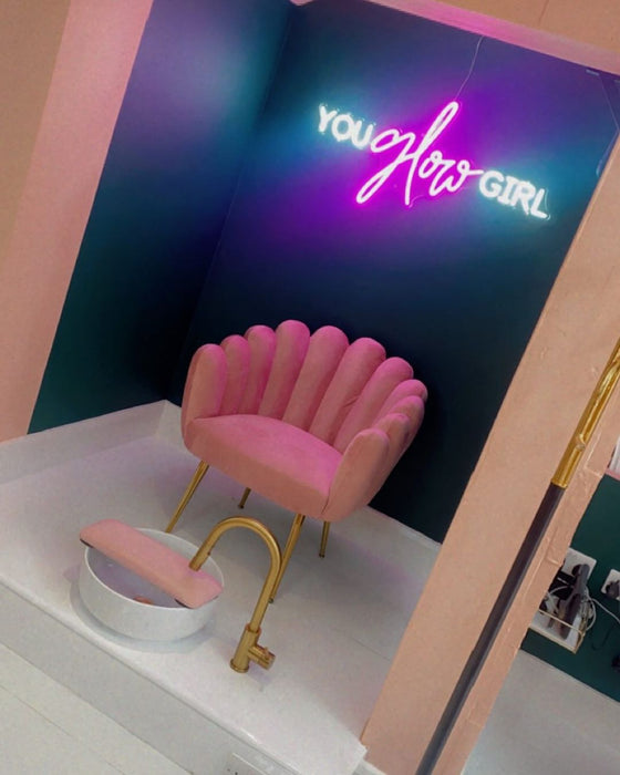 You glow girl neon sign in nail salon under pink scalloped chair and pedicure sink.