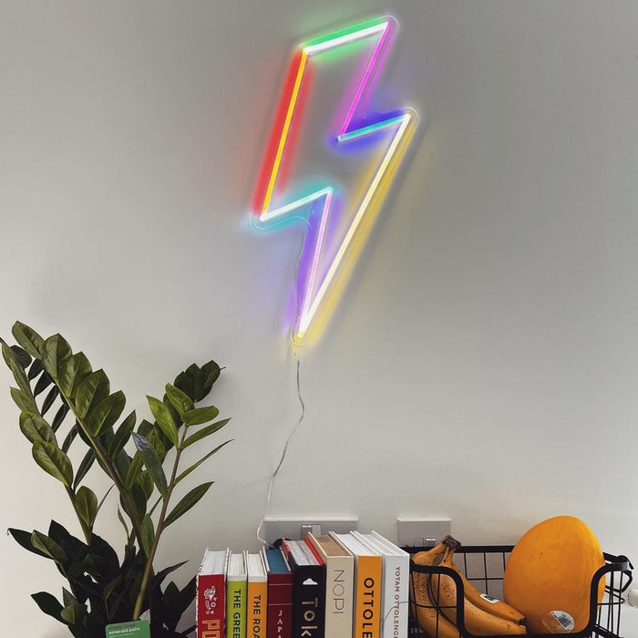 Lightning Bolt Neon Sign on white wall with plant and books. Photo by rachiepoos