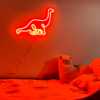 Bright orange single line Diplodocus Dinosaur Neon Sign mounted on the wall above a child's bed