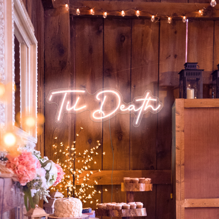 Til Death neon light in snow white against a wooden backdrop surrounded by wedding decorations