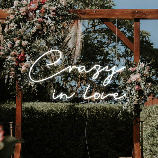 White crazy in love neon sign hanging against a botanical background