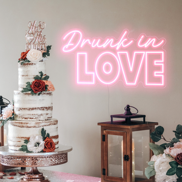 Pastel pink drunk in love neon sign behind a wedding cake