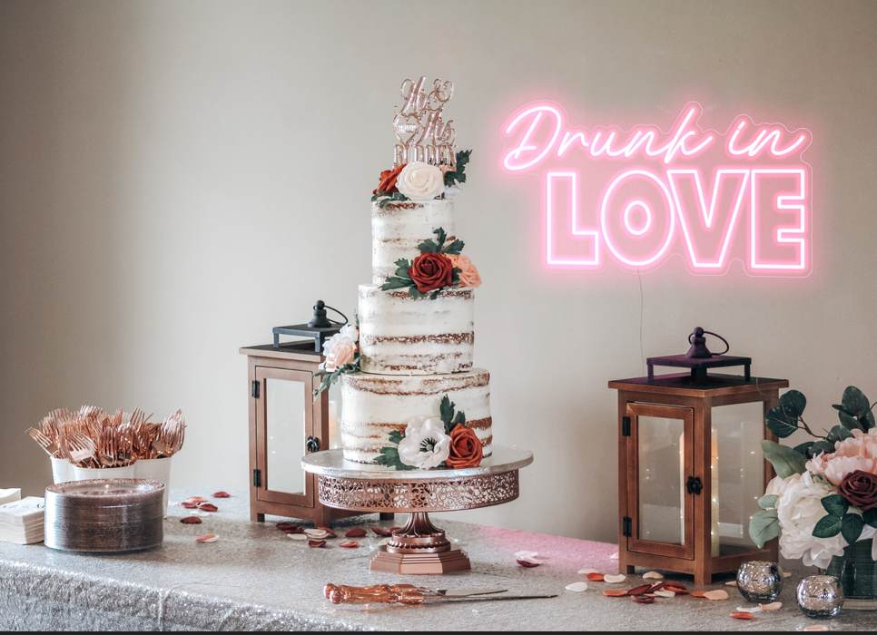 Pastel pink drunk in love neon sign behind a wedding cake